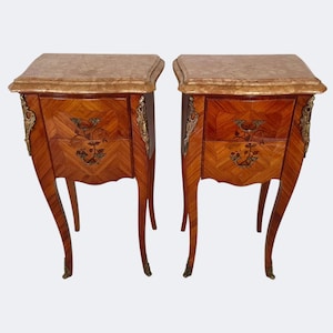 Puede incluir: Un par de mesitas de noche antiguas de madera. Cada mesa presenta una tapa de mármol, adornos de latón y un diseño de marquetería en los frentes de los cajones. Las mesas tienen patas curvas y son de color marrón cálido.
