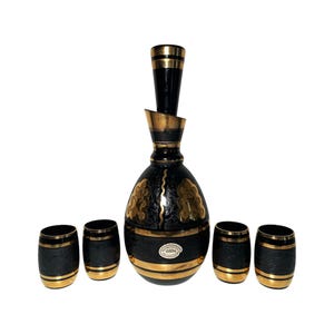 May include: A black and gold decanter set with four matching glasses. The decanter has a textured surface and gold accents. The glasses are also textured and have gold rims.