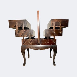 May include: Antique wooden sewing box with multiple drawers and a handle. The dark brown box sits on four curved legs. The drawers are secured with metal clasps. A vintage storage solution.