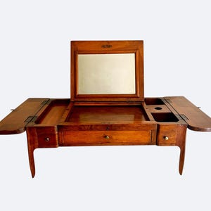 May include: A vintage wooden vanity with a rectangular mirror, drawers, and side compartments. The vanity has a warm brown finish, brass hardware, and a hinged top. The side panels are open. The vanity is on four curved legs.