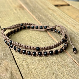 Peut inclure: Un bracelet en perles brunes et noires avec un cordon tressé. Le bracelet est fait de perles noires et d'un cordon brun tressé.