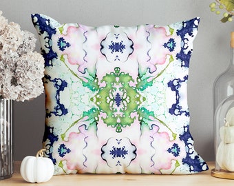 Può includere: Un cuscino decorativo con sfondo bianco e un design astratto colorato con sfumature di blu, verde e rosa. Il cuscino ha una forma quadrata ed è realizzato in tessuto morbido.
