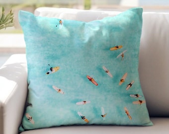 May include: A turquoise blue throw pillow with a pattern of people on surfboards in a turquoise blue ocean.