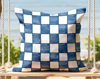 May include: A blue and white checkered throw pillow on a wooden swing hanging from a tree branch. The swing is in front of a beach scene.