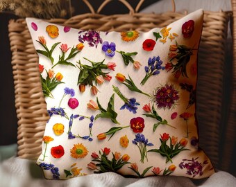 Könnte beinhalten: Ein weißes Kissen mit einem Blumenmuster, das verschiedene bunte Blumen zeigt, darunter Tulpen, Stiefmütterchen und Gänseblümchen. Das Kissen liegt auf einem Korbstuhl.