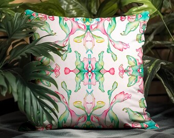 Può includere: Un cuscino bianco con un design astratto colorato con tonalità rosa, verdi e blu. Il design è simmetrico e ricorda un motivo floreale stilizzato.