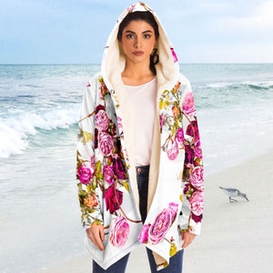 May include: A white hooded jacket with a floral print featuring pink, red, and green roses. The jacket has a sherpa lining and a long, flowing design.