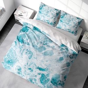 May include: A white duvet cover with a blue and white ocean wave pattern. The duvet cover is on a bed with two matching pillowcases.