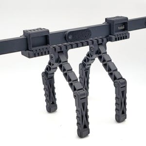 May include: Black adjustable tripod stand with a black bar and a Tobii logo. The bar has a small camera lens and a black cable attached.