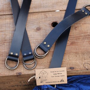 Puede incluir: Dos correas de cuero negro con anillas en D de lat&oacute;n y una etiqueta de papel marr&oacute;n que dice "Sangle de sac fourre-tout, Long 120 cm, Cuir/Tannage v&eacute;g&eacute;tal, Fabriqu&eacute; en Afrique par Jo."