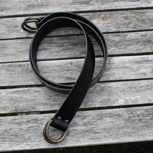 Puede incluir: Un cintur&oacute;n de cuero negro con una hebilla de doble anillo de lat&oacute;n.