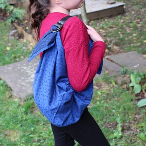 Puede incluir: Un bolso tote azul y negro con estampado y una correa de cuero marr&oacute;n. El bolso se lleva sobre el hombro de una persona que lleva un su&eacute;ter rojo y pantalones negros.