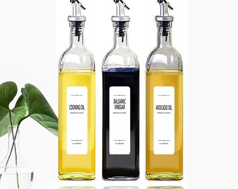 Puede incluir: Tres botellas de vidrio con boquillas de vertido y etiquetas. Las botellas están llenas de diferentes líquidos: aceite de cocina amarillo, vinagre balsámico negro y aceite de aguacate amarillo. Las etiquetas tienen los nombres de los líquidos impresos en ellas.