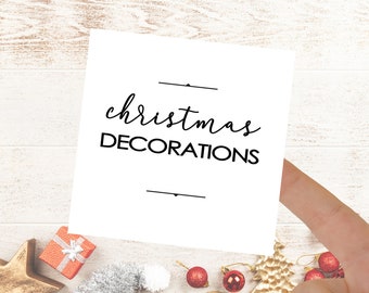 May include: White card with black text that reads "christmas decorations" on a white wood background with gold, silver, and red Christmas decorations.