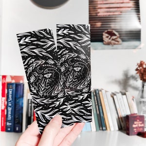 May include: Two black bookmarks with white illustrations of a cat, butterfly, and leaves. The bookmarks have the text "MOONCHILD" printed on them.