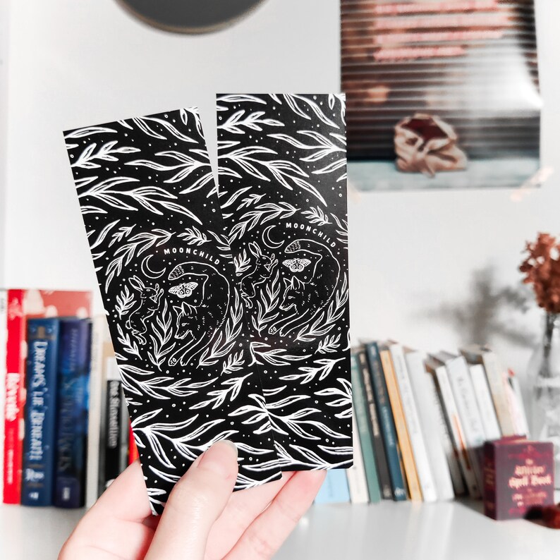 May include: Two black bookmarks with white illustrations of a cat, butterfly, and leaves. The bookmarks have the text "MOONCHILD" printed on them.
