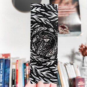 May include: Black and white bookmark with a stylized illustration of a wolf, a rabbit, and a moth. The text "MOONCHILD" is printed on the bookmark.