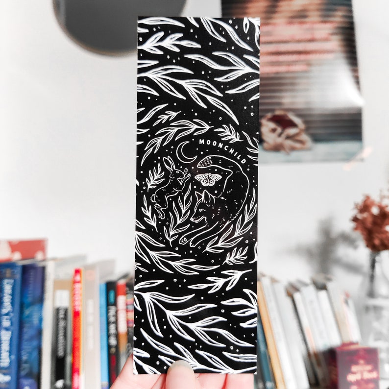 May include: Black and white bookmark with a stylized illustration of a wolf, a rabbit, and a moth. The text "MOONCHILD" is printed on the bookmark.