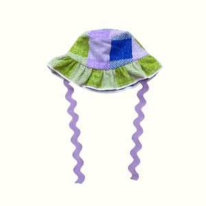 May include: A green, purple and blue plaid bucket hat with a ruffled brim and long, wavy purple ties.