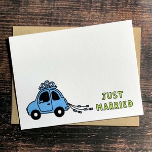 May include: A white card with a blue car with a white bow on top and the text "JUST MARRIED" in green letters.