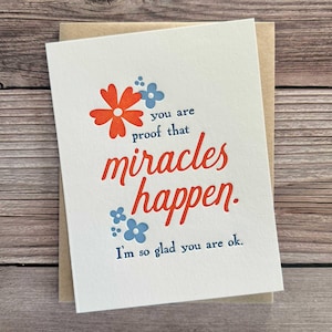 May include: A white card with a red flower and blue flowers printed on it. The card says "You are proof that miracles happen. I'm so glad you are ok."