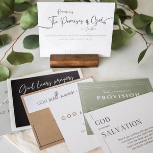 May include: A set of five cards with inspirational quotes about God's promises. The cards are in various colors, including black, brown, gray, and green. The cards are arranged on a white surface with a wooden stand holding a card that reads "Remembering The Promises of God in Scripture".