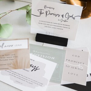 May include: A set of cards with inspirational quotes about God's promises. The cards are printed on different colored paper with a variety of fonts and designs. The cards are arranged on a white surface with a wooden sculpture and a green plant.