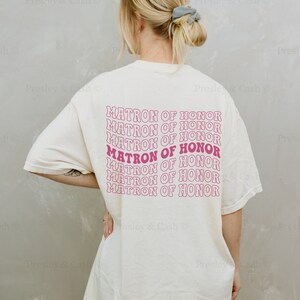 K&ouml;nnte beinhalten: Ein wei&szlig;es T-Shirt mit dem Text "MATRON OF HONOR", der in rosa Schrift auf dem R&uuml;cken wiederholt wird. Das Shirt ist &uuml;berdimensioniert und das Model tr&auml;gt es locker.