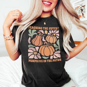 May include: Black t-shirt with a fall-themed graphic. The design features pumpkins, flowers, and the text "TEACHING THE CUTEST PUMPKINS IN THE PATCH". The shirt is a size Large.