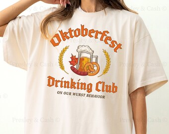 May include: Ivory-colored oversized t-shirt with the text "Oktoberfest Drinking Club" in orange. The graphic includes a beer stein, pretzel, and leaf. The shirt is a 2XL size.