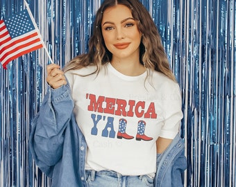 May include: A woman wearing a white t-shirt with the text "'MERICA Y'ALL" and a red, white, and blue boot graphic. She is holding a small American flag in her right hand. She is wearing a denim jacket and blue jeans. The background is a blue and silver tinsel curtain.