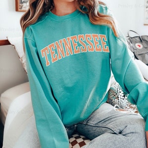 Op de afbeelding: Seafoam groene trui met het woord "TENNESSEE" in oranje en witte letters. De trui is maat L.