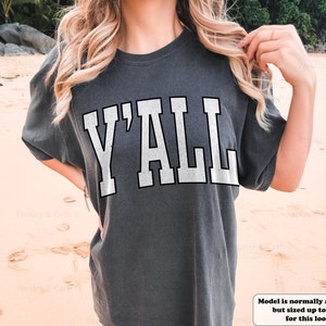May include: A gray t-shirt with the word "Y'ALL" printed in white on the front. The model is wearing a size XL, but normally wears a medium.