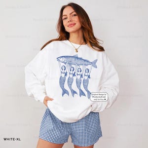 Peut inclure: Sweat-shirt blanc avec un motif bleu de quatre sir&egrave;nes tenant un poisson. Le texte "Original design by Presley And Cash only on Etsy" est imprim&eacute; dans le coin inf&eacute;rieur droit du sweat-shirt.
