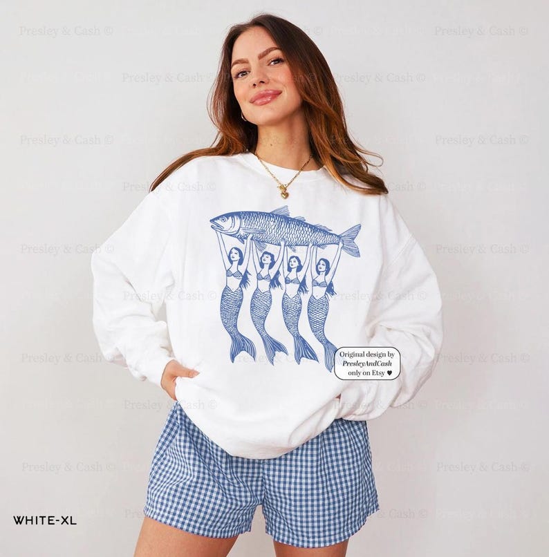 Peut inclure: Sweat-shirt blanc avec un motif bleu de quatre sir&egrave;nes tenant un poisson. Le texte "Original design by Presley And Cash only on Etsy" est imprim&eacute; dans le coin inf&eacute;rieur droit du sweat-shirt.