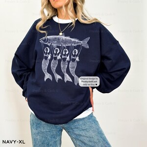 Peut inclure: Sweat-shirt bleu marine avec un motif blanc de quatre sir&egrave;nes tenant un poisson. Le texte "Original design by PresleyAndCash only on Etsy" est imprim&eacute; sur le sweat-shirt.