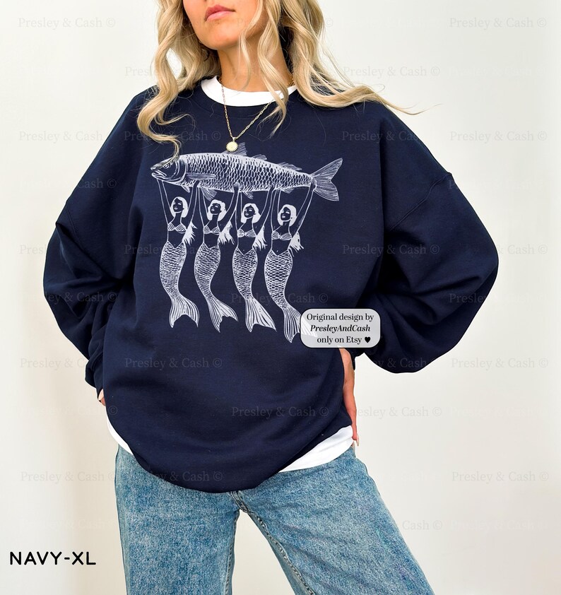 Peut inclure: Sweat-shirt bleu marine avec un motif blanc de quatre sir&egrave;nes tenant un poisson. Le texte "Original design by PresleyAndCash only on Etsy" est imprim&eacute; sur le sweat-shirt.