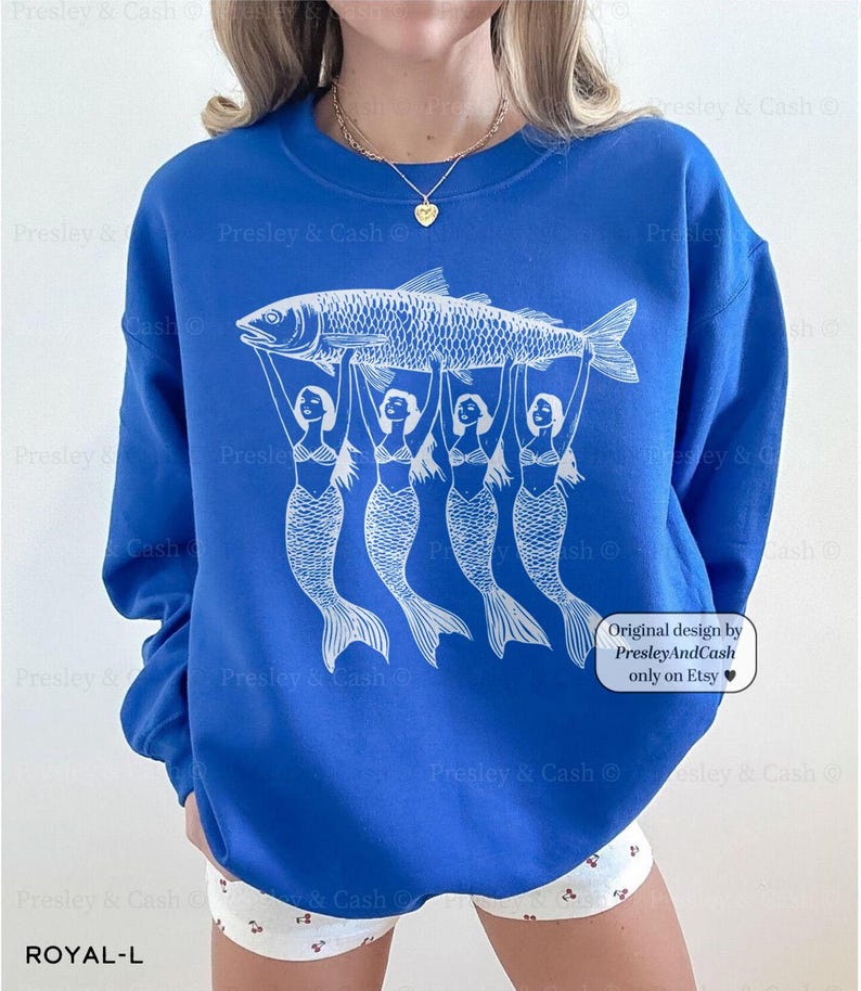 Peut inclure: Un sweat-shirt bleu royal avec un motif blanc de quatre sir&egrave;nes tenant un poisson. Le texte "Original design by PresleyAndCash only on Etsy" est imprim&eacute; dans le coin inf&eacute;rieur droit du sweat-shirt.