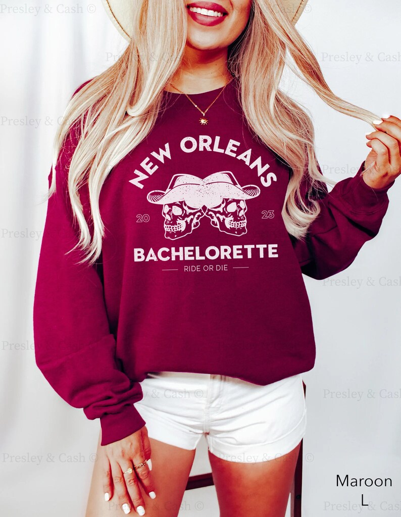 Peut inclure: Sweat-shirt bordeaux avec un imprim&eacute; graphique blanc de deux cr&acirc;nes portant des chapeaux de cow-boy avec le texte "NEW ORLEANS 20 23 BACHELORETTE RIDE OR DIE"