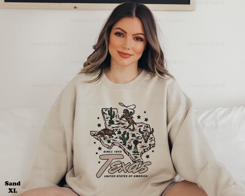 May include: Sand-colored XL sweatshirt featuring a graphic of the Texas state map with cacti, a cowboy, and longhorn. The text "Texas" and "United States of America" are below the map. The sweatshirt has the text "Since 1845".
