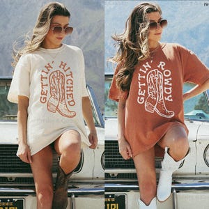May include: Ivory and yam-colored t-shirts with the text "GETTIN' HITCHED" and "GETTIN' ROWDY" printed on them, each featuring a cowboy boot graphic. The shirts are size L.