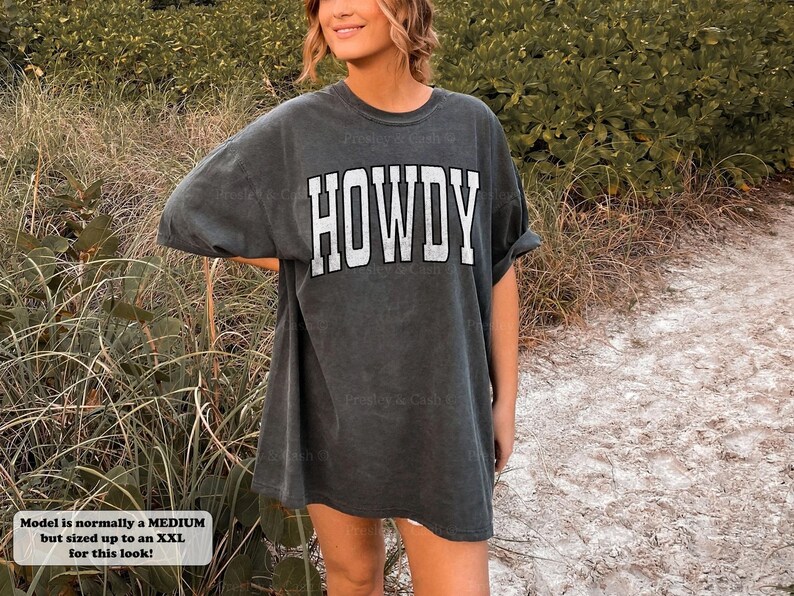 May include: A dark gray oversized t-shirt with the word "HOWDY" printed in white on the front. The model is wearing the shirt with a relaxed fit.