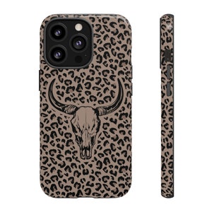 May include: A brown and black leopard print phone case with a black and white bull skull graphic. The case is designed for an iPhone.