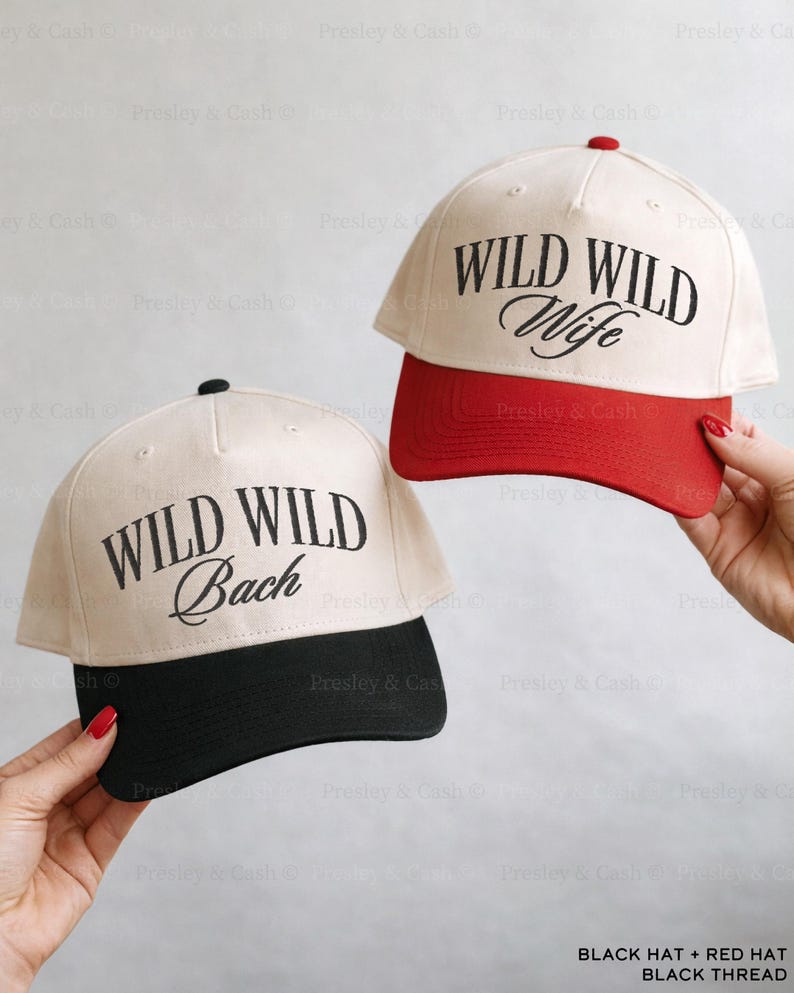 May include: Two baseball caps with the text "WILD WILD Bach" and "WILD WILD Wife" in black script. One cap has a black brim, the other a red brim. Both caps have a cream-colored crown and a black top button.