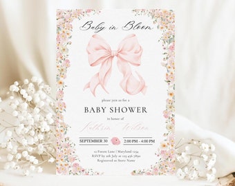 Puede incluir: Una invitación de baby shower rosa con un borde floral y un gran lazo rosa. El texto dice "Baby in Bloom" e incluye la fecha, la hora y la ubicación del evento.