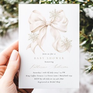 May include: A baby shower invitation with a cream and beige watercolour bow and snowflake design. The invitation includes the text "Join us for a Baby Shower" and event details, such as the honoree's name, date, time, and location.