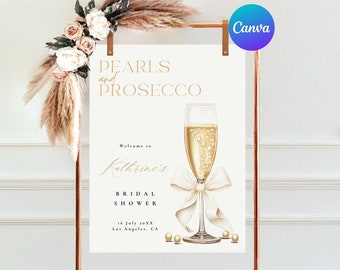 May include: A sign for a bridal shower with the text "Pearls and Prosecco." The sign features a champagne glass with a white bow and pearls. The sign is displayed on a copper-colored stand and decorated with flowers.