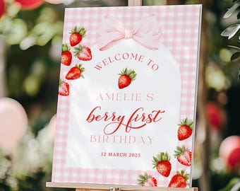 May include: Pink and white gingham welcome sign with a pink bow and red strawberries. The sign says "Welcome to Amelie's Berry First Birthday 12 March 2025".