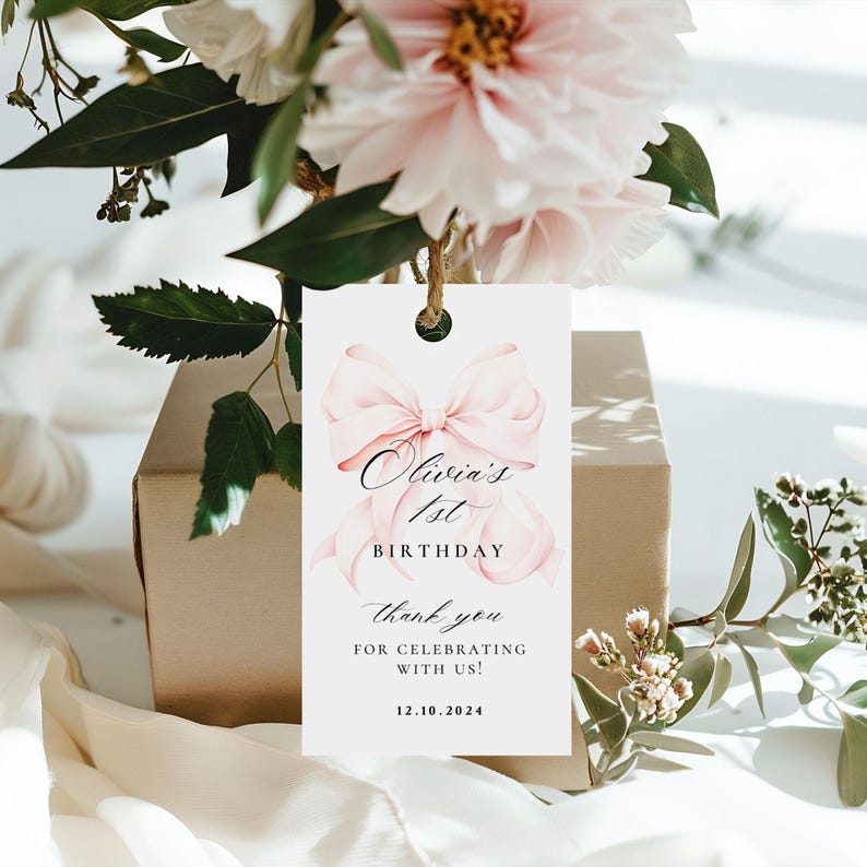 Pode incluir: Uma etiqueta de agradecimento branca com um la&ccedil;o rosa de aquarela e o texto "Olivia's 1st Birthday" e "Thank you for celebrating with us! 12.10.2024".