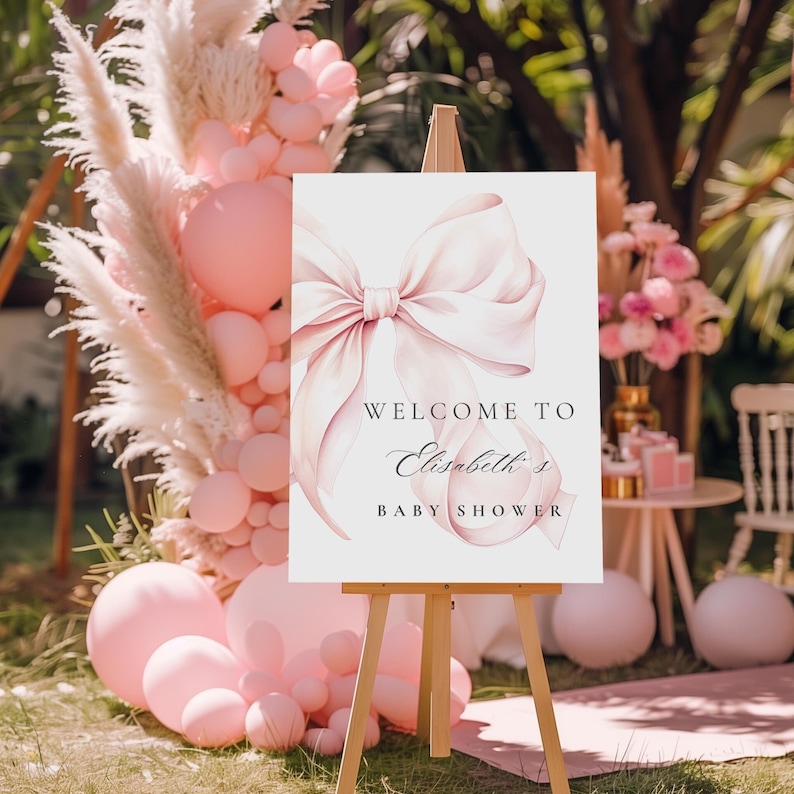 K&ouml;nnte beinhalten: Ein wei&szlig;es Willkommens-Schild mit einer rosa Aquarell-Schleife und dem Text "Willkommen zu Elizabeths Baby Shower".